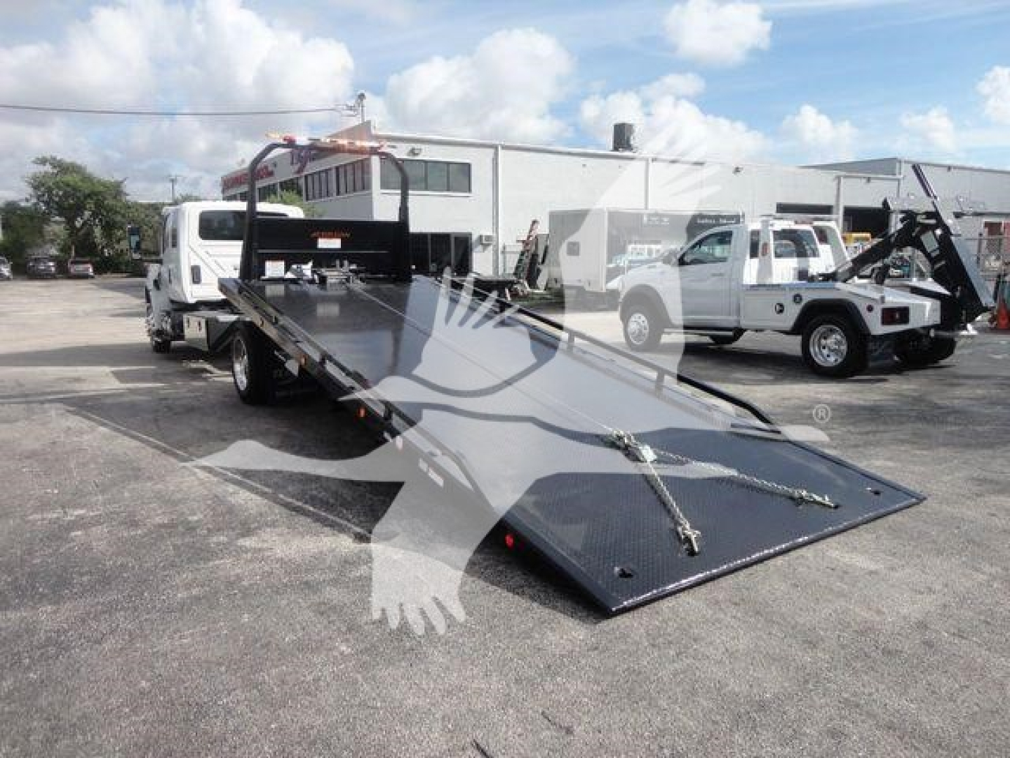 Truck bed with a lowered deck in a flatbed rollback tow truck setup; appears to be a new International MV roll-back with a long black metal platform and side rails.