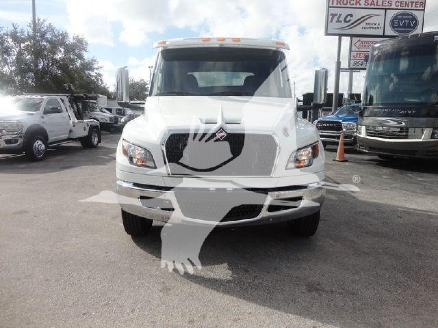 Truck front view showing 2027 International MV with large grille, dual headlights, and side mirrors in a lot with other trucks.