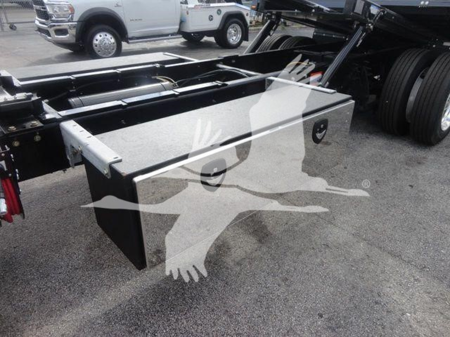 Truck rollback bed toolbox with silver metallic lid and black body mounting, International MV chassis visible in background.