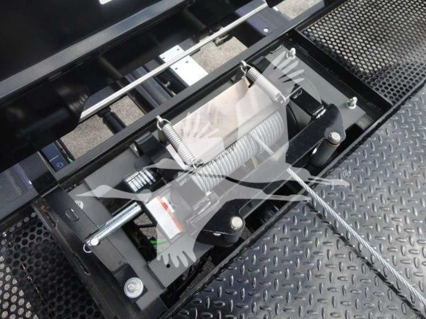 Trailer hitch/rollback equipment with visible spring loaded mechanism and chain on a diamond plate surface.