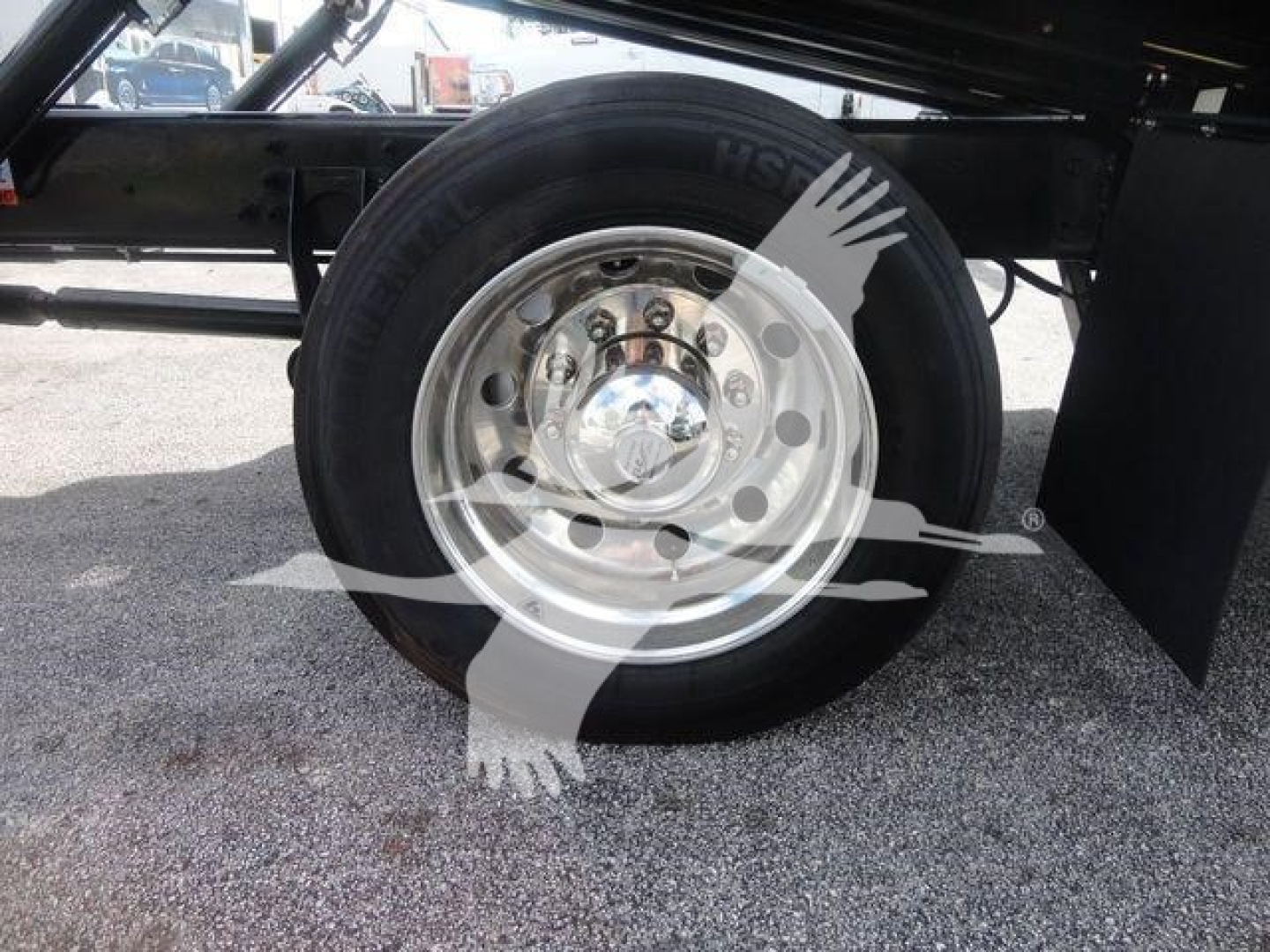 Wheel and tire close-up on a trailer axle with polished steel rim and black tire, undercarriage visible.