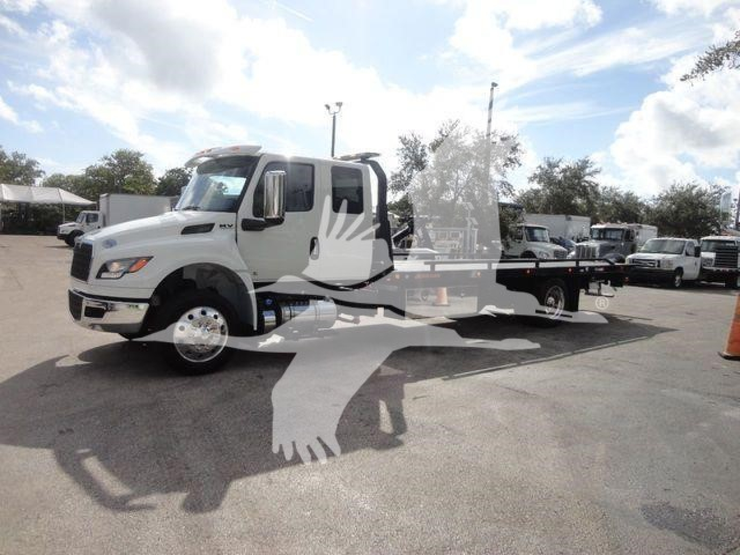 International MV truck in a dealership lot, white cab with flatbed rollback equipment and a watermark of a bird graphic over the image.