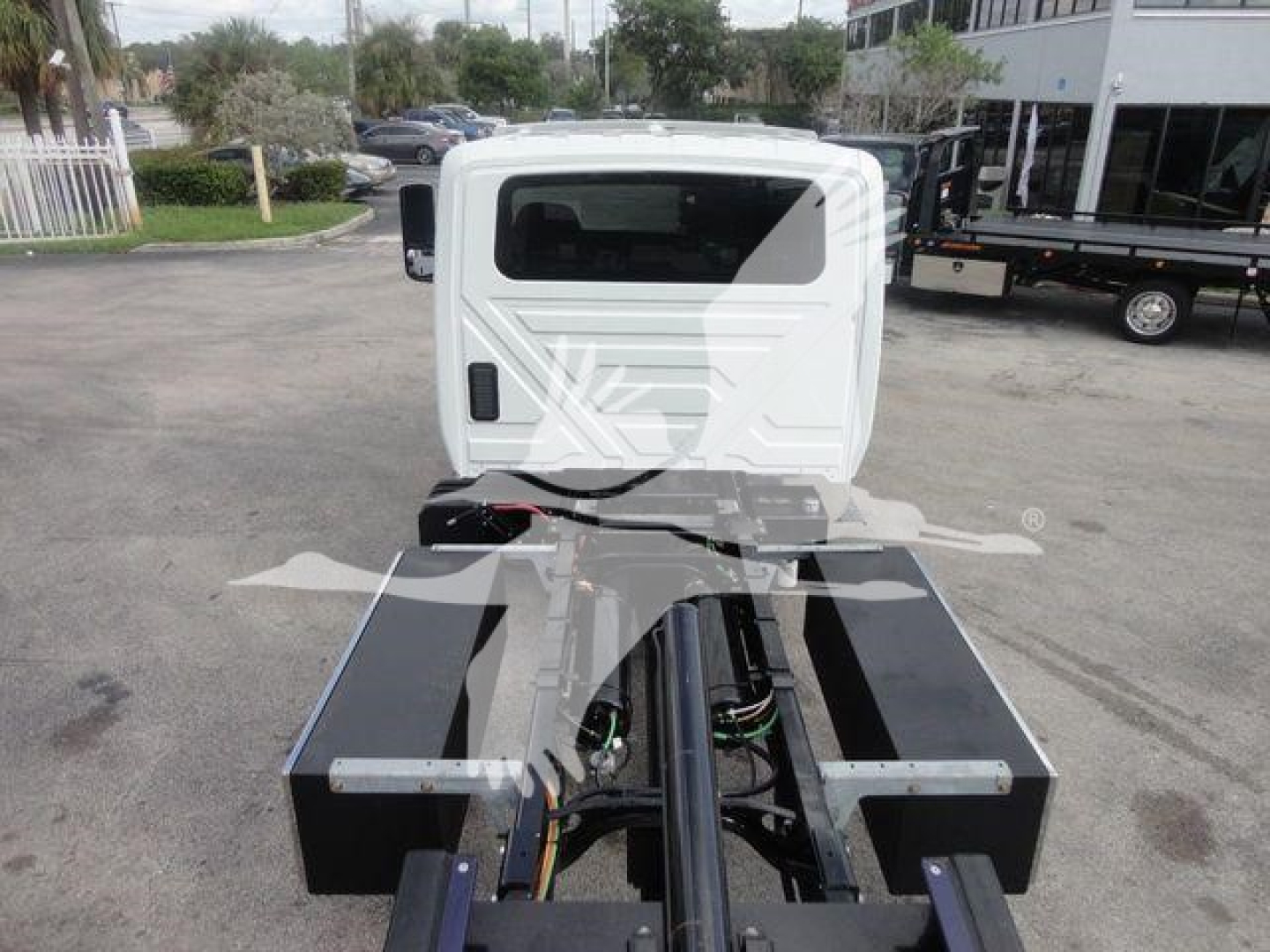 Truck cab rear view showing heavy-duty hitch/boom frame with hydraulic lines and control levers in a rollback truck configuration.