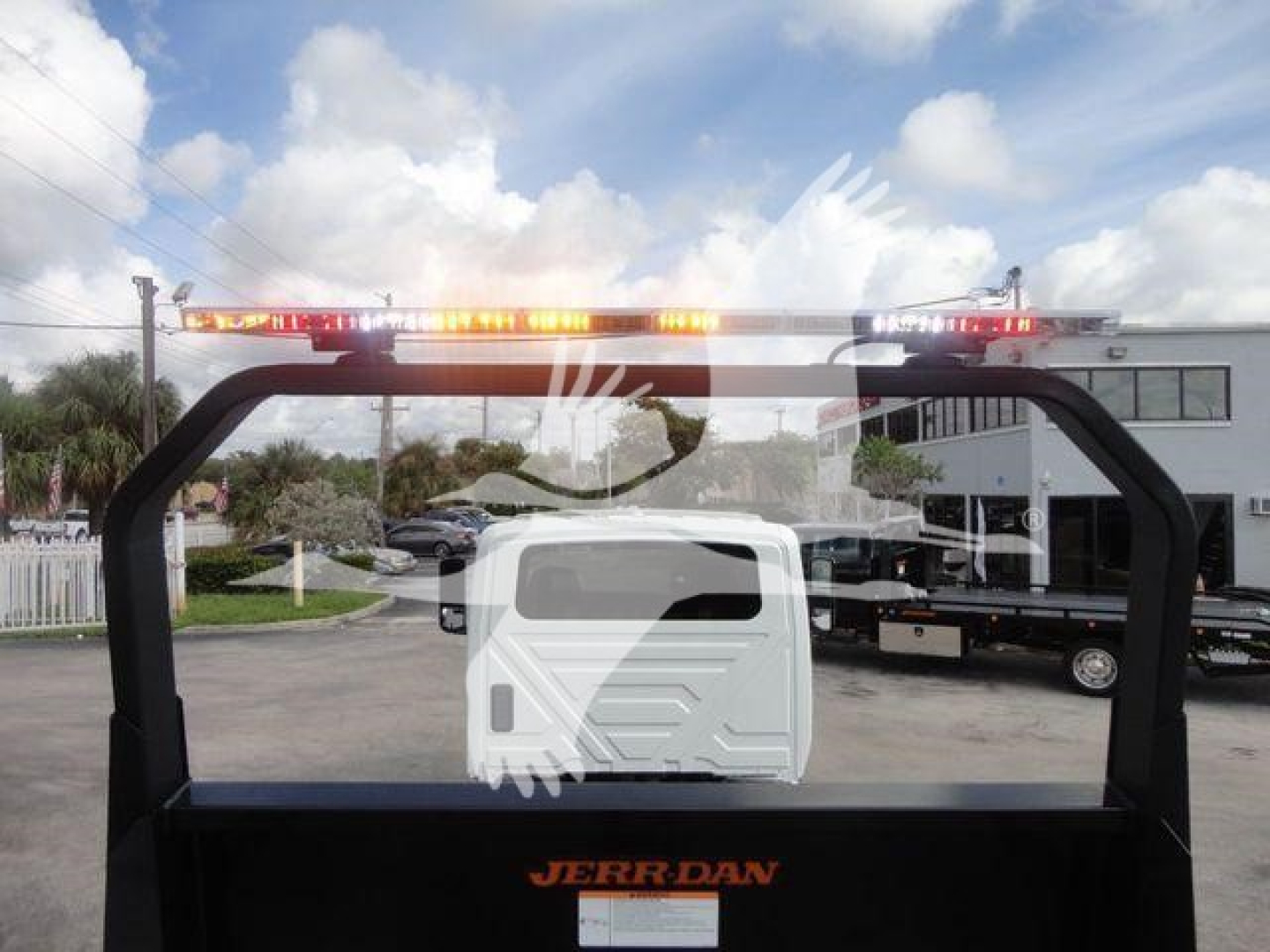 Truck bed with hydraulic rollback equipment and orange warning lights on top; rear window shows reflection of surroundings; JERRDAN branding on the bed.