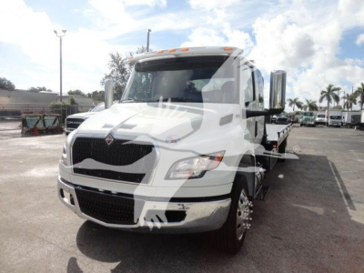 White 2027 International MV rollback tow truck front view with black grille and chrome bumper, cab interior visible, dealership lot in background.
