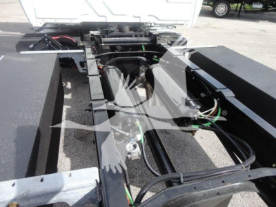 Truck chassis and cab area showing wiring, hydraulic lines, and frame rails of a new International MV rollback truck.