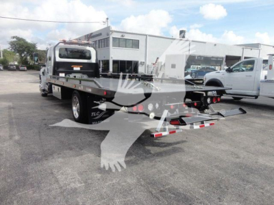 Flatbed rollback tow truck rear view showing reflective tape and wheel wells. Visible text on truck includes TLC branding on wheel arch and platform.