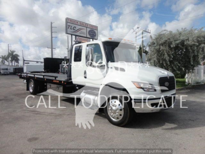 Flatbed tow truck from International MV series with stock number MV607EXCAB22XLP, visible dealership sign in background.