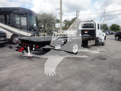 Flatbed tow truck in a dealership lot showing MV607EXCAB22XLP International MV chassis and trailer bed with side rails.