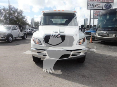 Truck front view showing 2027 International MV with large grille, dual headlights, and side mirrors in a lot with other trucks.