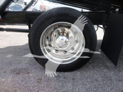 Wheel and tire close-up on a trailer axle with polished steel rim and black tire, undercarriage visible.