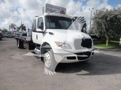 International MV truck cab and flatbed trailer viewed from front-right, white exterior with black grille, showing equipment badge and headlights.