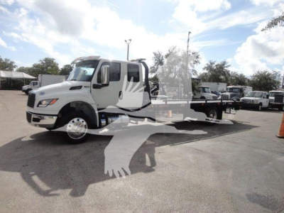International MV truck in a dealership lot, white cab with flatbed rollback equipment and a watermark of a bird graphic over the image.