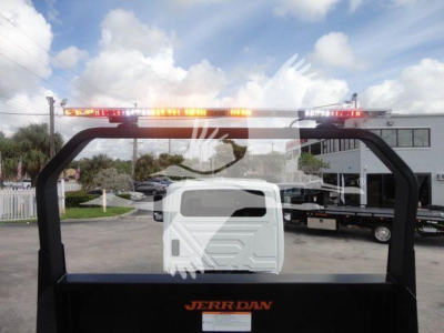 Truck bed with hydraulic rollback equipment and orange warning lights on top; rear window shows reflection of surroundings; JERRDAN branding on the bed.