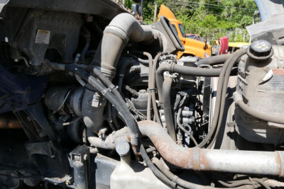 Truck engine bay view showing various hoses, pipes, and components of an International Prostar+ 122 engine with metal tubing and black plastic wiring harnesses.