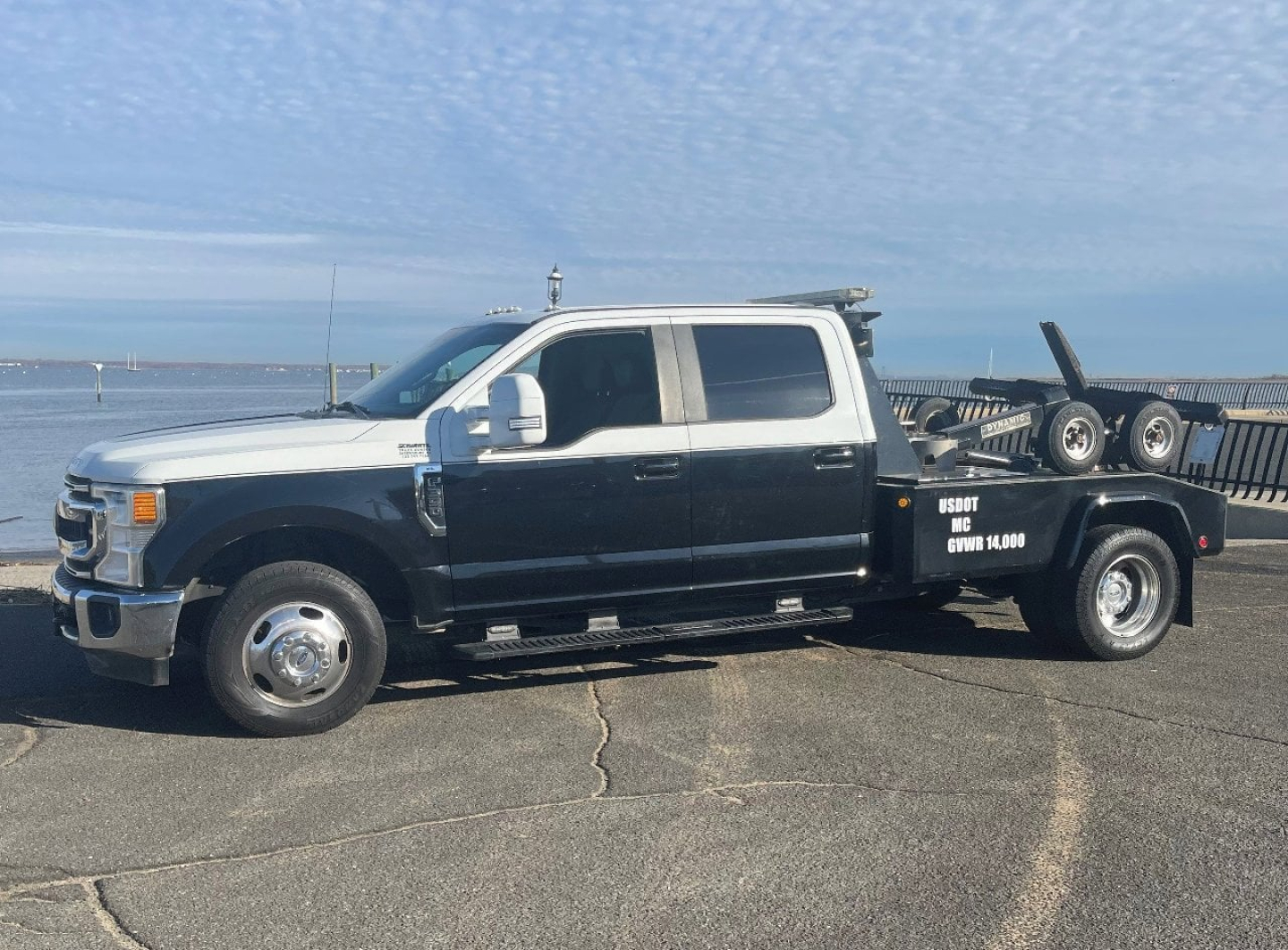 2020 Ford Super Duty F-350 DRW tow truck side view showing dual-tone white cab and black flatbed with equipment rack and text on bed.