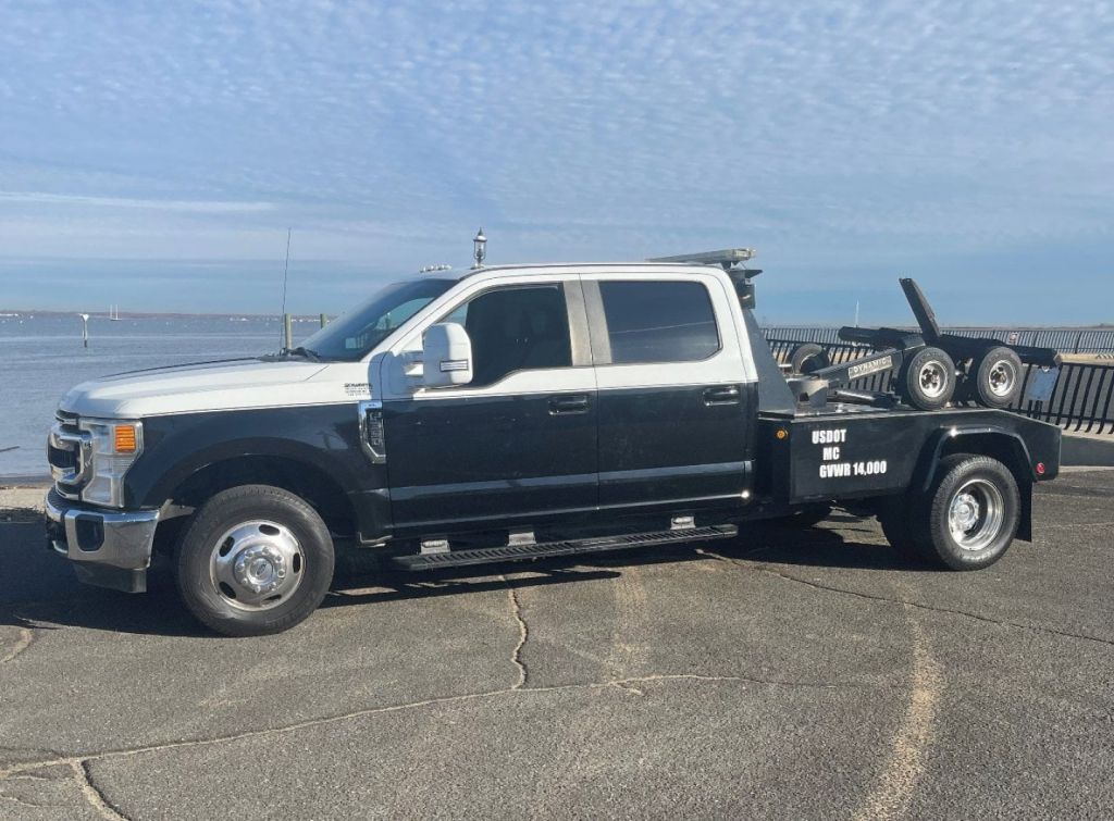 2020 Ford Super Duty F-350 DRW tow truck side view showing dual-tone white cab and black flatbed with equipment rack and text on bed.