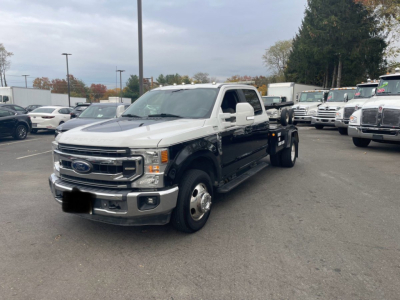 Ford F-350 tow truck chassis cab dual rear wheel with white cab and black flatbed. Front grille shows Ford logo. Visibility of other trucks in lot.