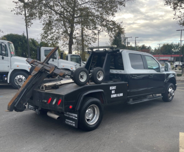 Tow truck with flatbed and wheel lift on a 2020 Ford F-350 DRW, black and white, in a dealership lot.