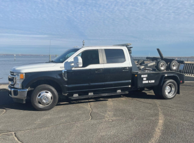 2020 Ford Super Duty F-350 DRW tow truck side view showing dual-tone white cab and black flatbed with equipment rack and text on bed.