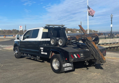 Ford F-350 Super Duty tow bed truck side view showing heavy-duty rear hoist and wheel chocks with white cab and black body.