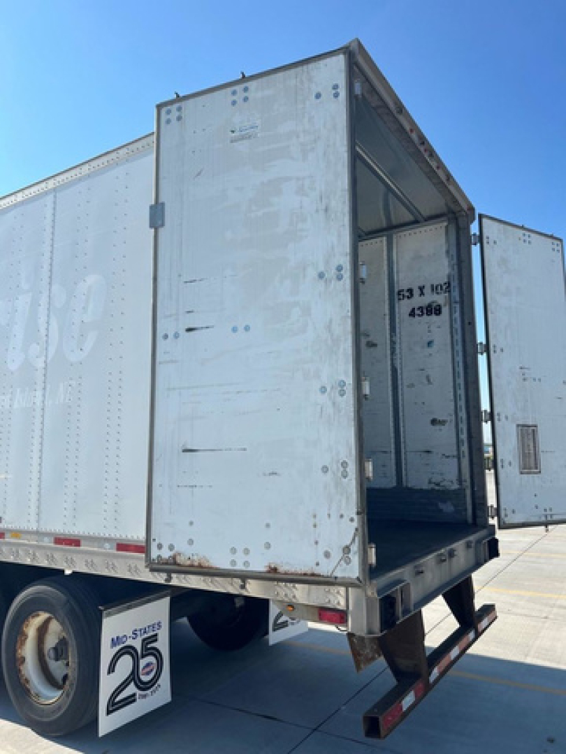 Trailer rear with open dual doors showing cargo area of a white utility van trailer. Visible text includes MO-STATE 26 wheel chock and interior markings.