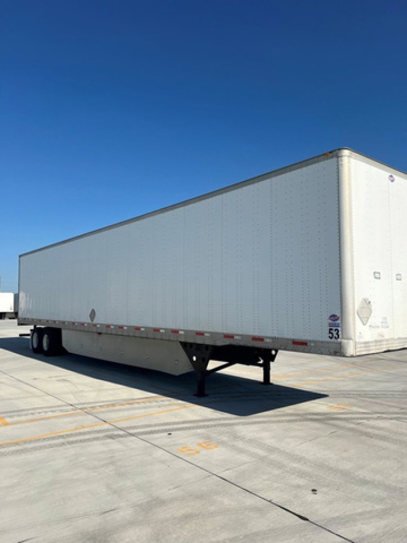 Trailer van showing box structure with dual rear axles, white exterior, and wheel area.