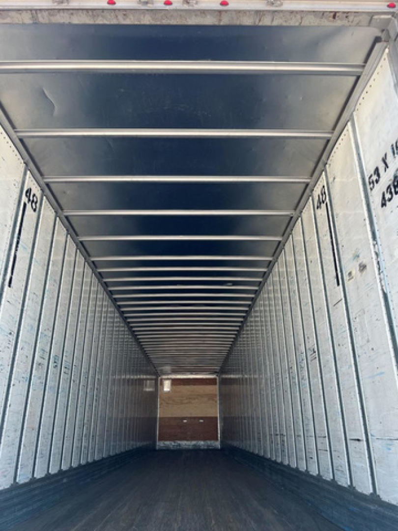 Van trailer interior showing empty metal walls and ceiling ribs; dark floor at far end.