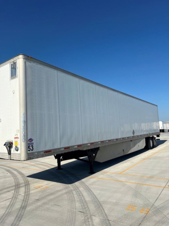 Trailer van side view showing aluminum box trailer with landing gear and wheel axles, numbered 53 near rear, under clear blue sky.