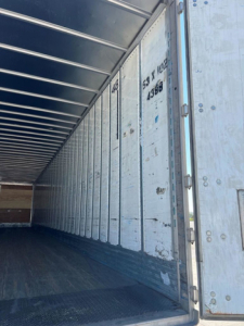 Trailer interior showing cargo area with metal side walls and flooring, vertical numbers and stamps on the panel.