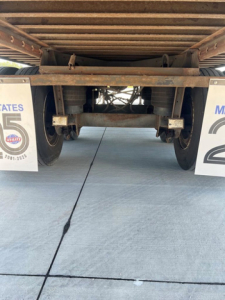 Underbody of a utility van/trailer showing rear axle and suspension; signs on both sides partially visible with text '5' and 'MATE'