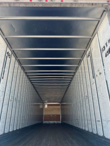Van trailer interior showing empty metal walls and ceiling ribs; dark floor at far end.