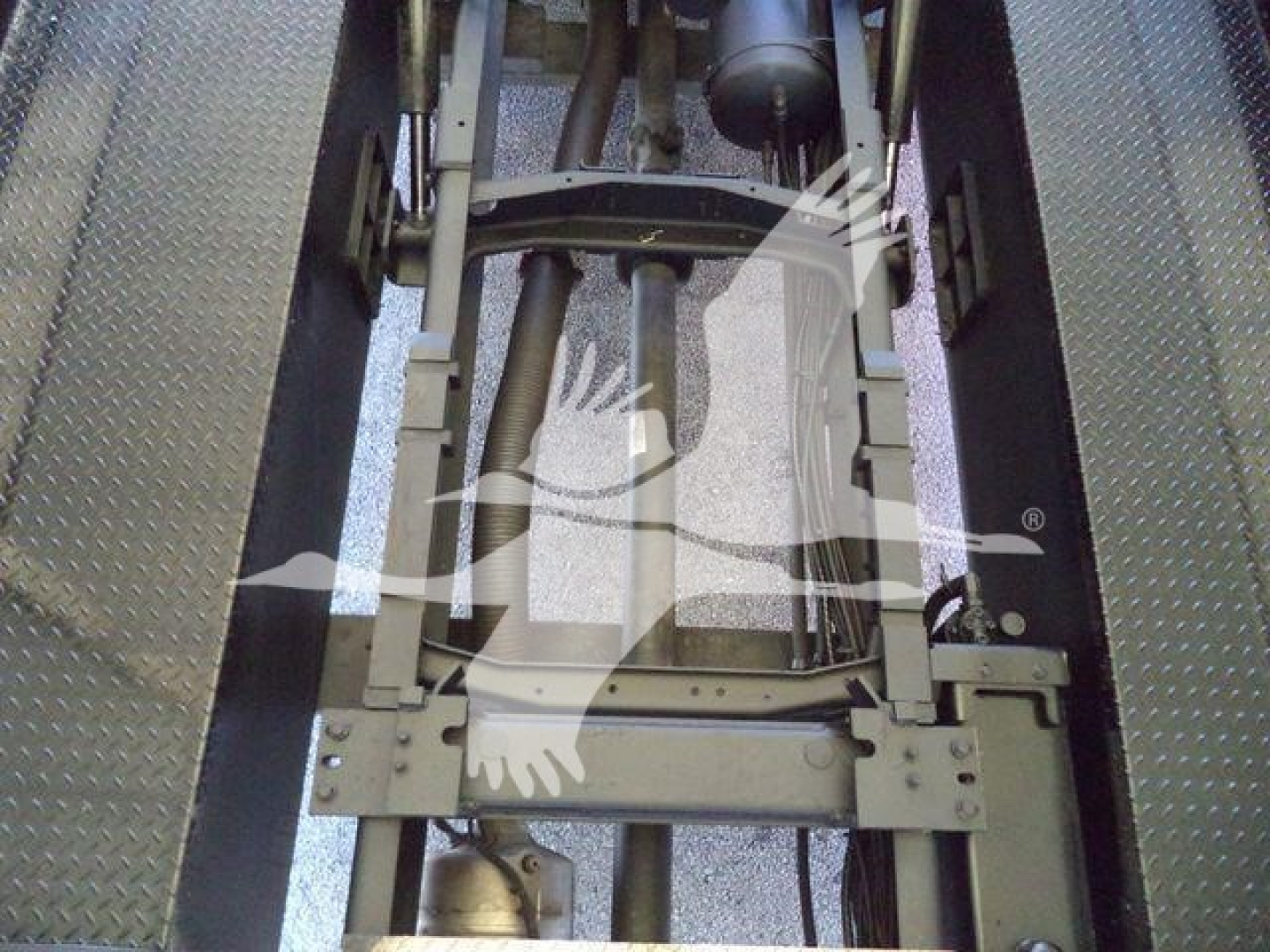 Truck chassis frame and hydraulic components inside a Mack MD6 rollback bed showing structural beams and hydraulic cylinders.