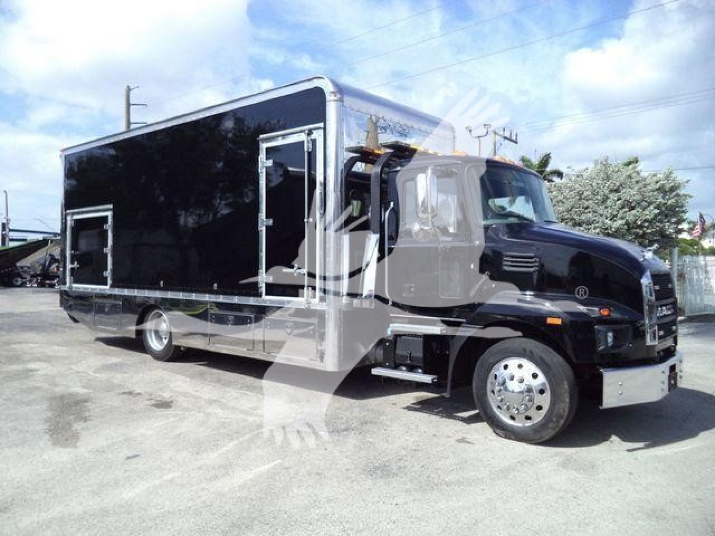 Truck with black utility body, cab shows Mack MD6 style with chrome bumper; side text not legible; image shows a large rollback/utility truck.
