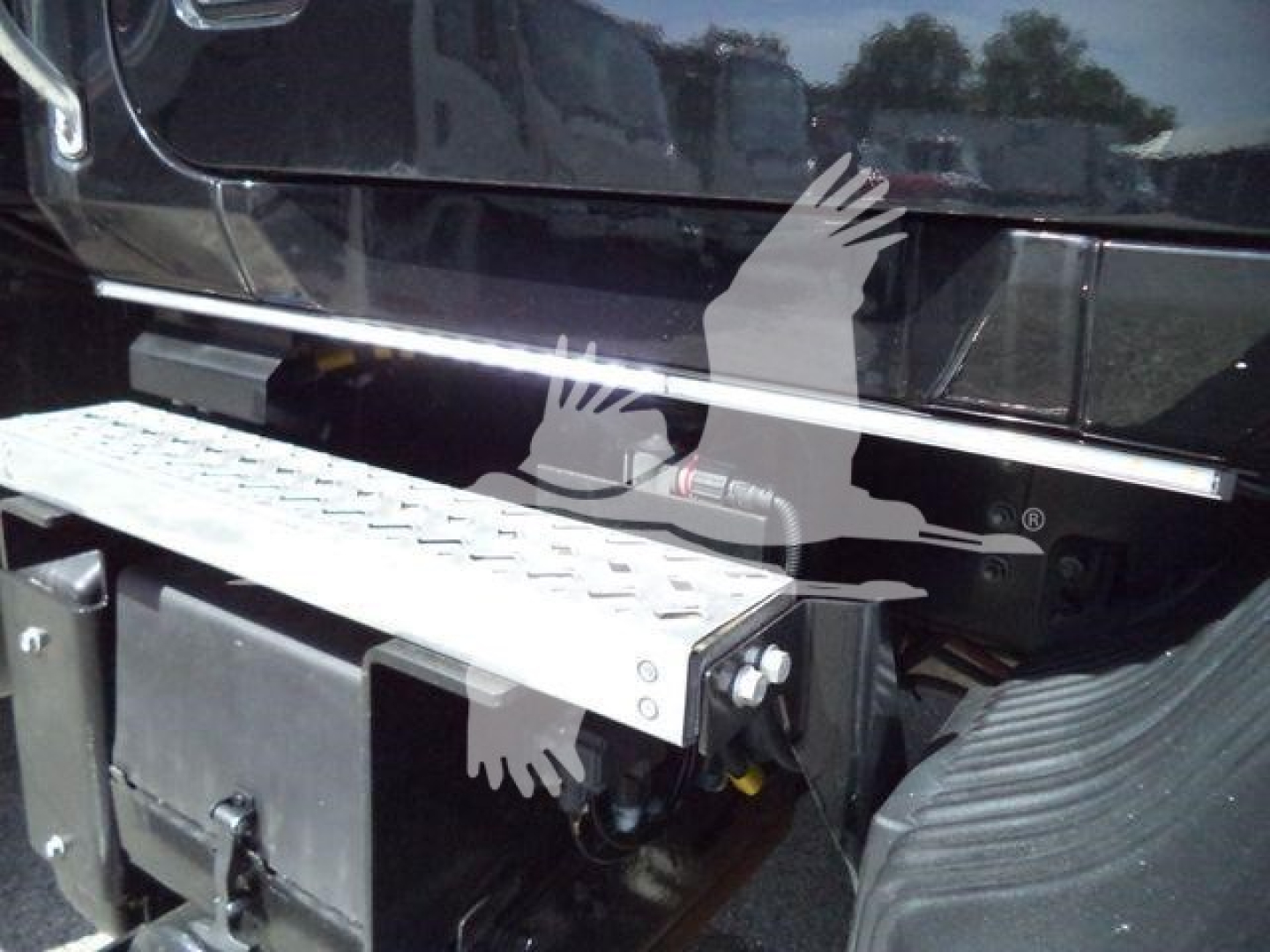 Step access plate and rear bumper area of a Mack MD6 rollback truck showing metal step with bolts and a black rear panel.