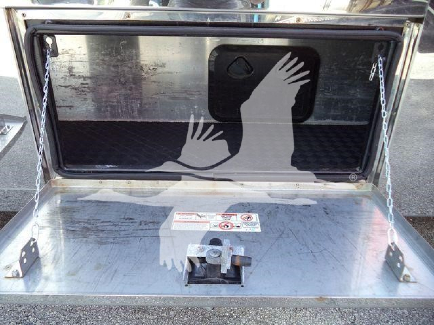 Trunk of a 2022 Mack MD6 rollback truck showing a metal storage compartment with a hinged lid, chain supports, and a warning label on the interior surface.