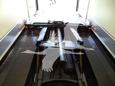 Truck bed or rollback chassis with hitch and hydraulic components visible in a reception area; metal platform and cylindrical piston visible.