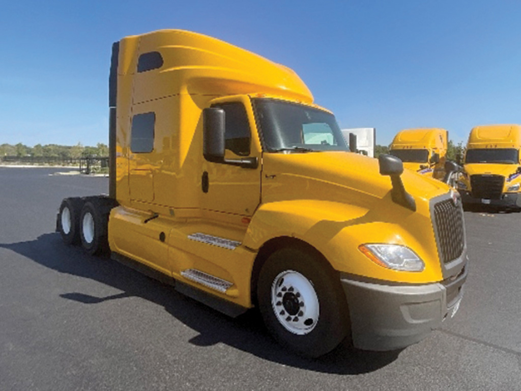 Truck cab in service view showing bright yellow 2022 International LT625 sleeper tractor with aerodynamic hood and side steps.