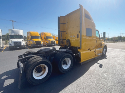 Truck tractor side view showing yellow sleeper cab with dual rear axles and attached fifth wheel in a used truck lot.