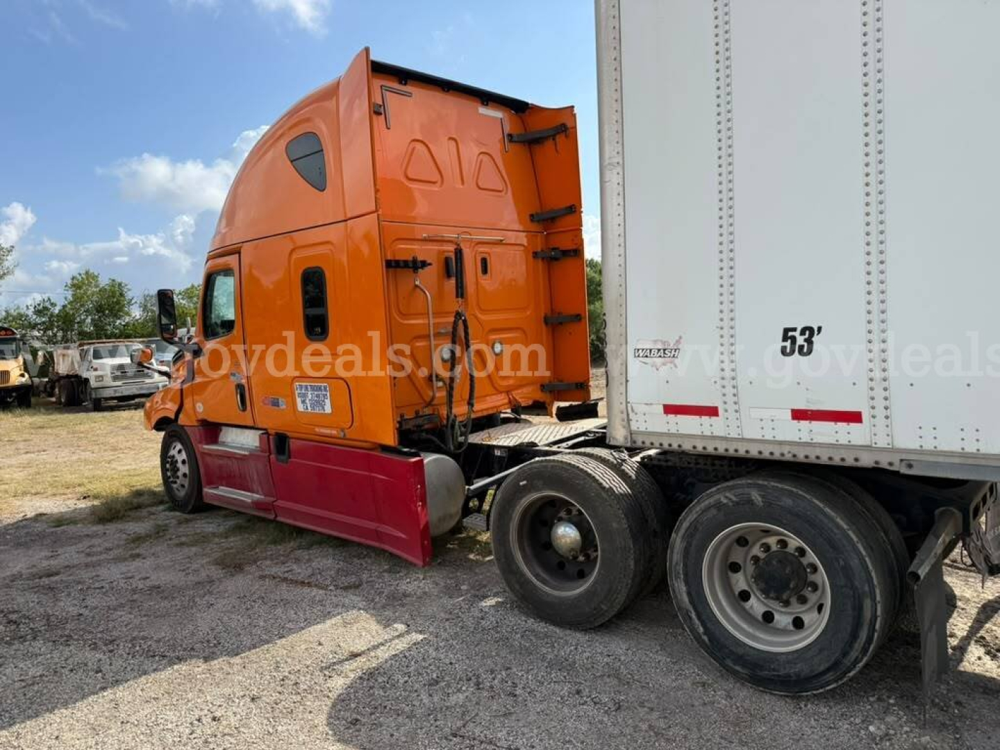 Truck cab and attached trailer of a 2020 Freightliner Cascadia with orange cab and red side skirt, rear view showing 53' trailer and rear wheels.