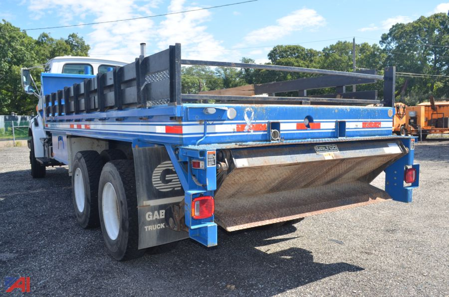 Flatbed truck with blue bed and hydraulic roll-off lift showing rear view and bumper hardware.