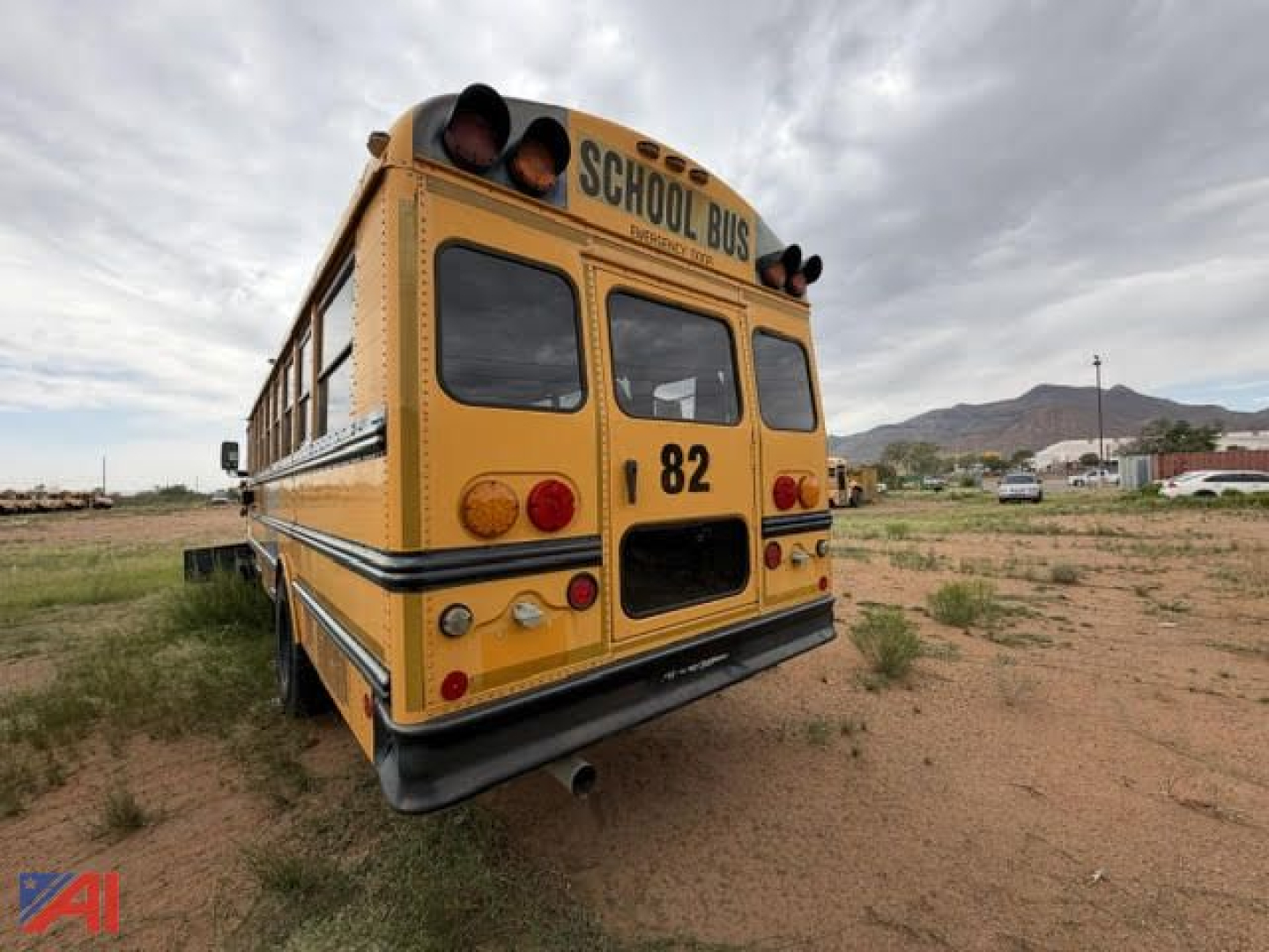 Rear view of a yellow Freightliner FS65 school bus with 'SCHOOL BUS' sign, number 82, dual rear lights, brake lights, and exhaust on a dirt lot.