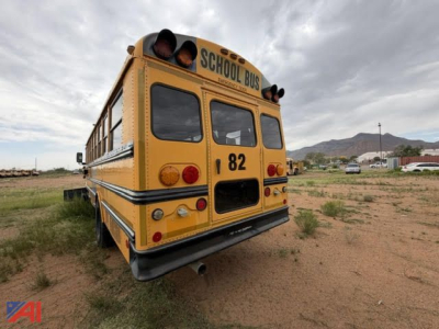 Rear view of a yellow Freightliner FS65 school bus with 'SCHOOL BUS' sign, number 82, dual rear lights, brake lights, and exhaust on a dirt lot.