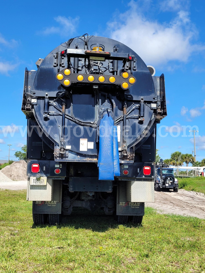 Rear view of a Mack GU713 vacuum truck showing mounting platform, rear lights, and hoses.