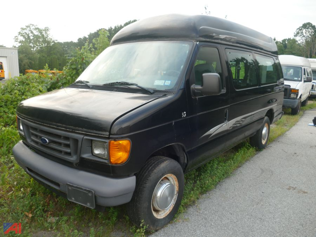 Ford E-250 van with wheelchair lift in a parking lot, black exterior, extended body, front grille and headlights visible.
