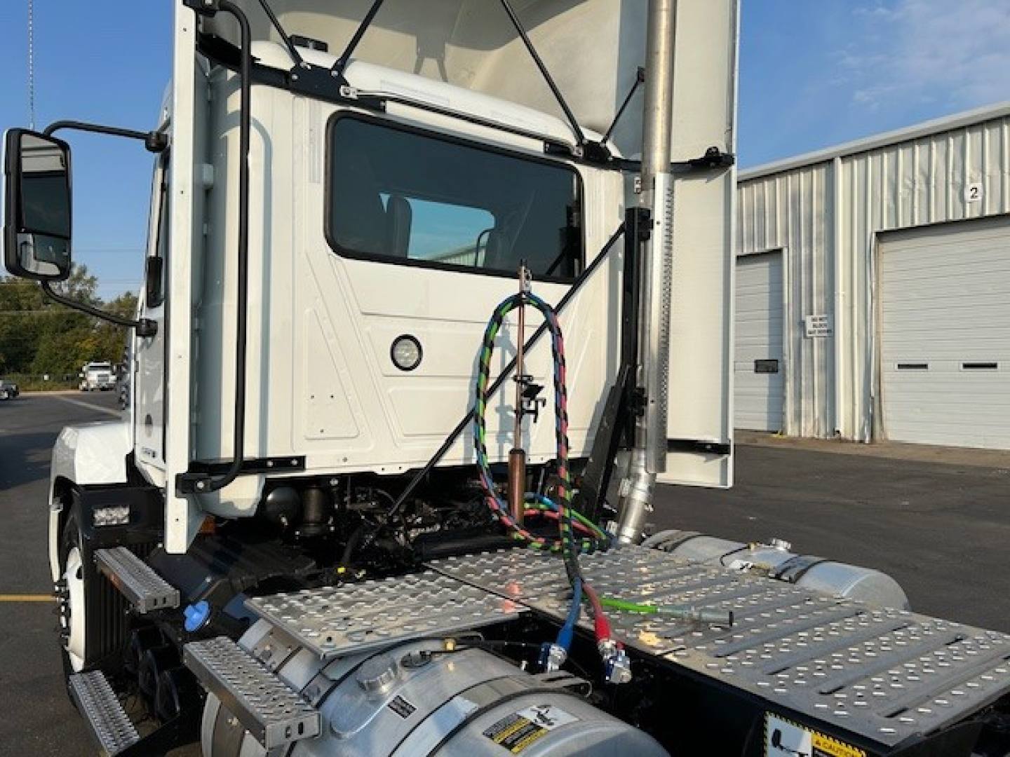 Truck cab and chassis showing intake pipes and diamond plate steps of a white 2025 Mack AN64T conventional daycab.