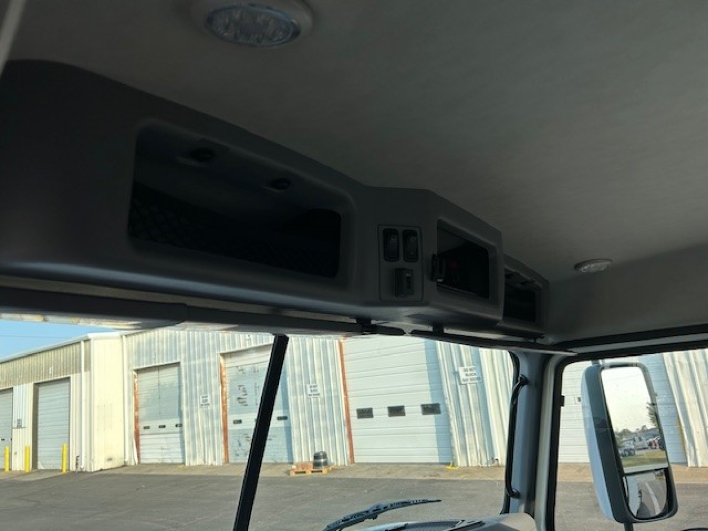 Cab interior roof area of a 2025 Mack AN64T daycab showing overhead storage compartments and controls.