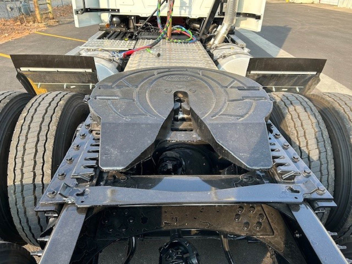 Rear view of a Mack AN64T daycab chassis showing fifth wheel and drivetrain components, dual rear axles, and exposed wiring harnesses.