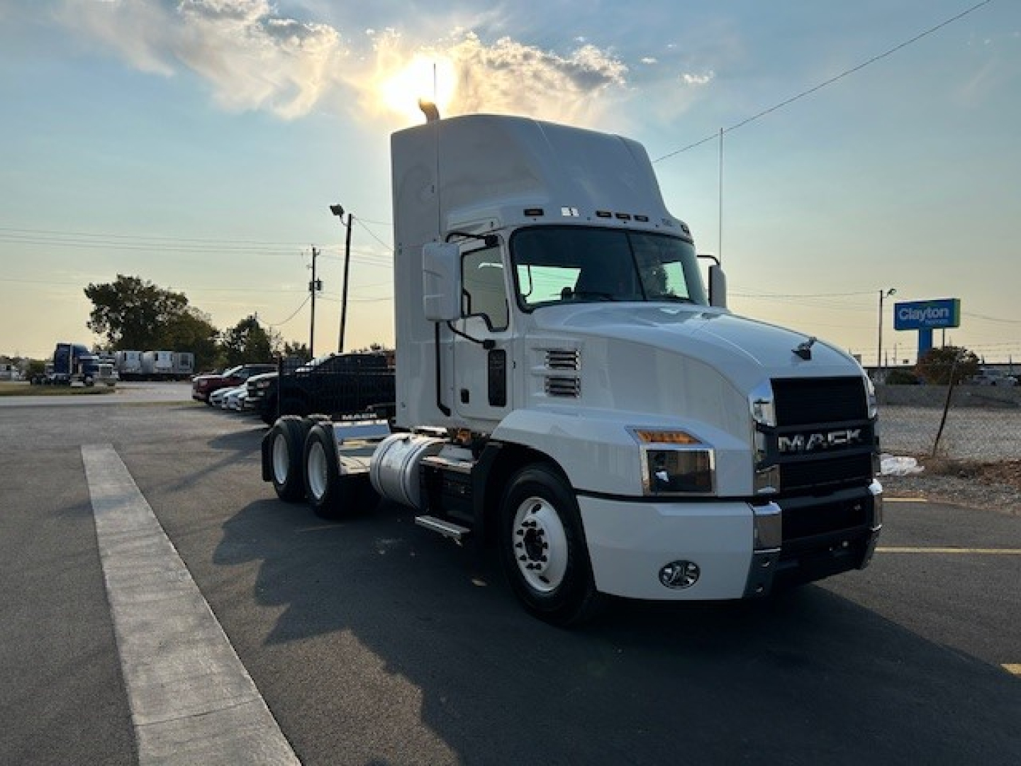 Truck cab showing 2025 Mack AN64T conventional daycab with white exterior, angled view, front grille with MACK emblem, side fuel tanks, and dual rear axles.