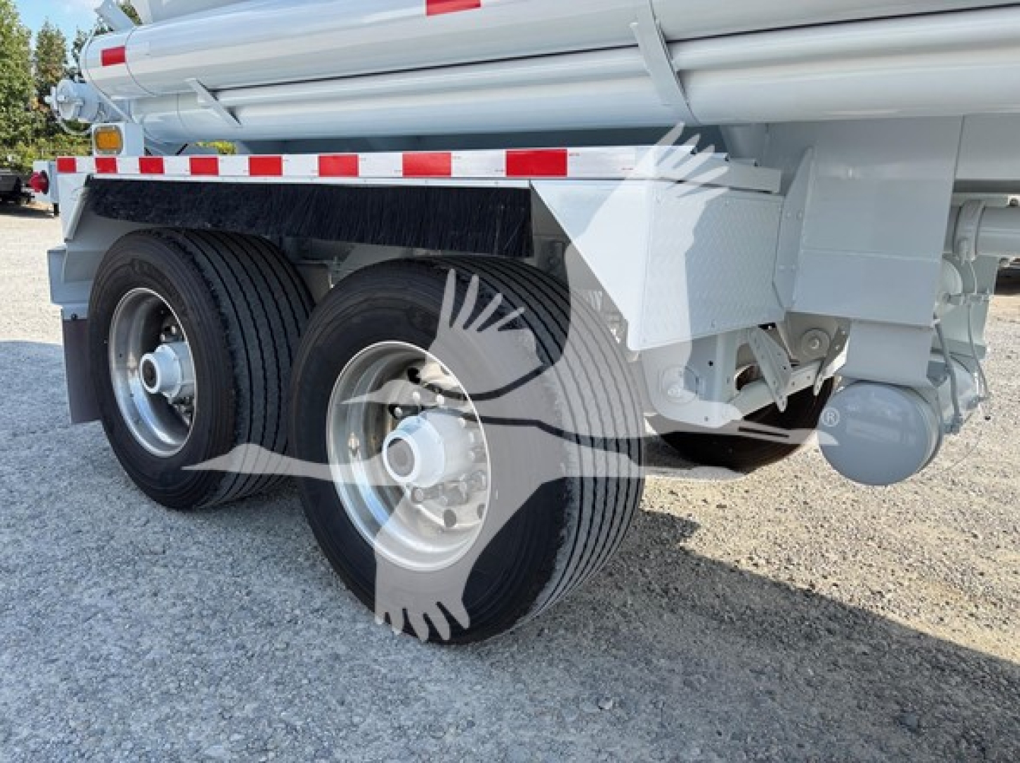Trailer axle showing dual rear tires and tanker body with reflective safety stripe and mudguard.